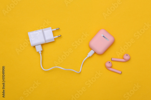 Wireless headphones with charging case and charging adapter on yellow background. Top view