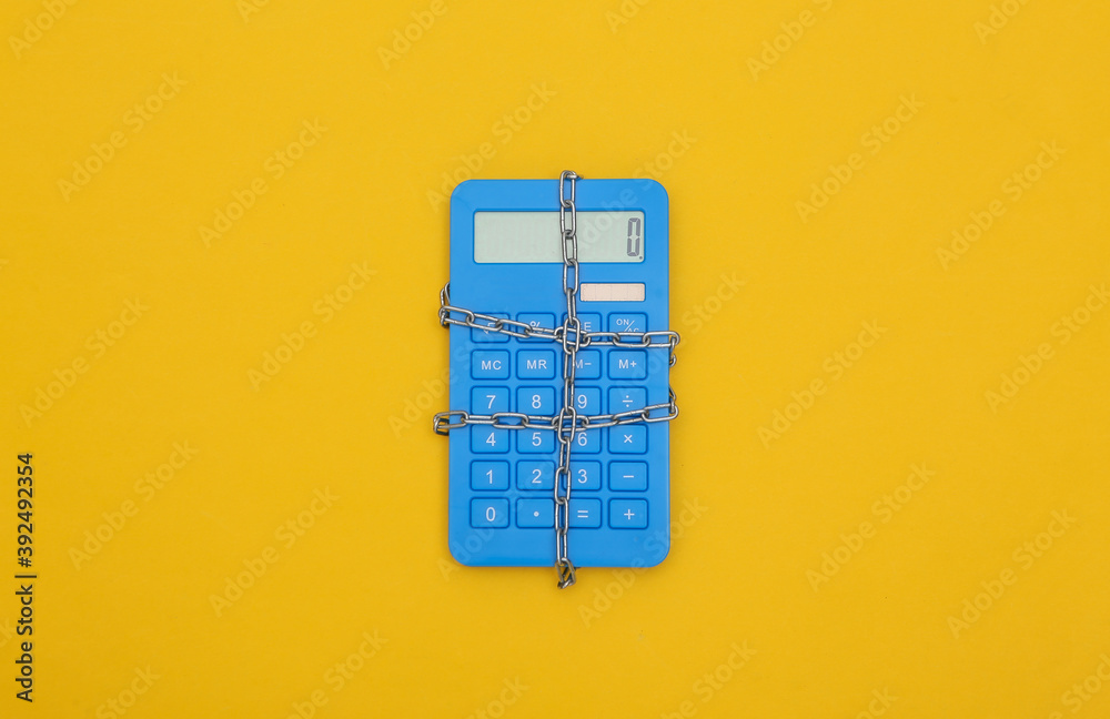 Blue calculator wrapped in steel chain on a yellow background. Top view Blue calculator wrapped in steel chain on a yellow background. Top view
