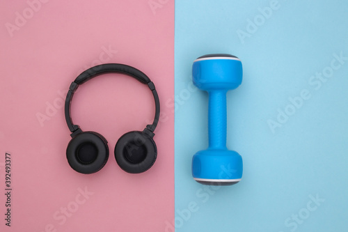 Dumbbell and stereo headphones on blue pink background. Sport concept. Top view