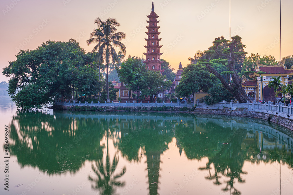 Obraz premium Hanoi buddhist pagoda (Tran Quoc Pagoda) on West Lake at Hanoi, colorful sunset, illuminated temple, water reflection. Vietnam travel.