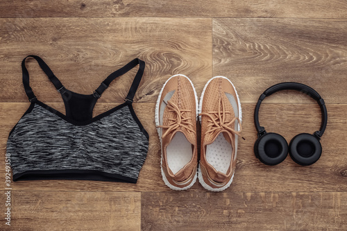 Sports shoes, top bra and stereo headphones on wooden background. Getting ready for training. Top view. Flat lay