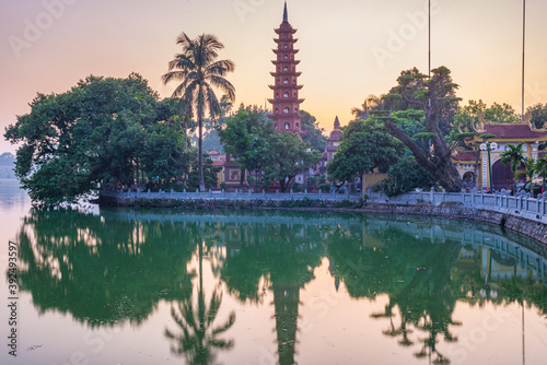 Hanoi buddhist pagoda (Tran Quoc Pagoda) on West Lake at Hanoi, colorful sunset, illuminated temple, water reflection. Vietnam travel.