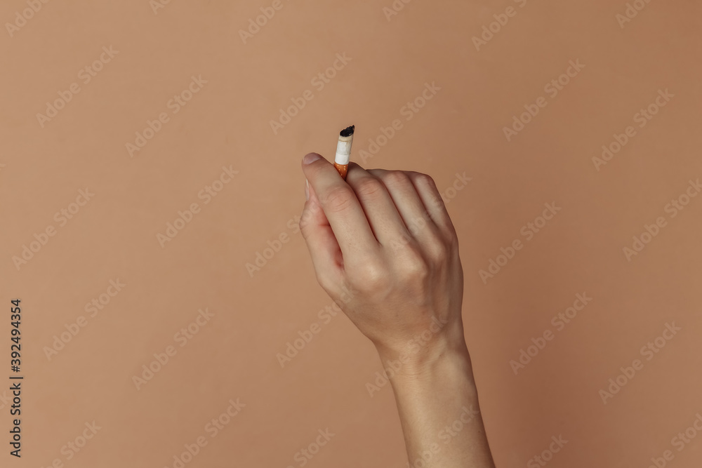 Female hand holding cigarette on brown background Female hand holding cigarette on brown background