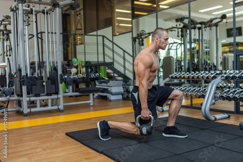 Workout-focused muscular sculpted man exercising with a kettlebell in modern gym. Bodybuilding strength training