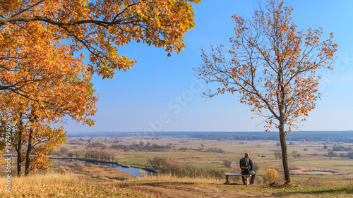 Autumn landscape - view of the hiker sitting on a bench overlooking a river valley on a sunny day, the northeast of Ukraine