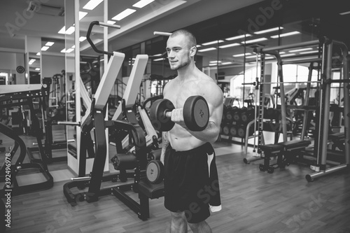 Concentrated on workout muscular lean man exercising with dumbbells in modern gym. Biceps pumping