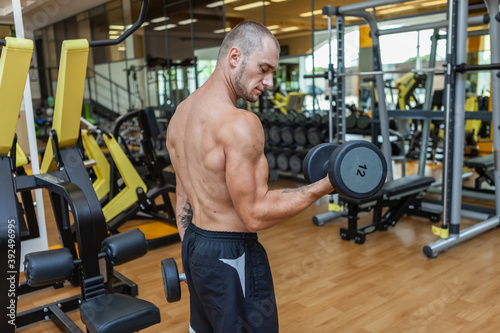 Concentrated on workout muscular lean man exercising with dumbbells in modern gym. Biceps pumping