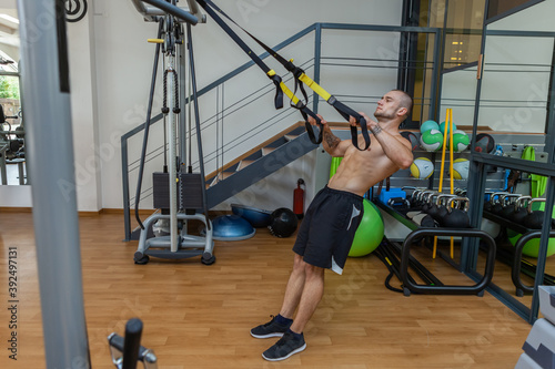 Muscular naked torso man training with fitness trx system in the gym. Bodybuilder exercising his muscles with suspension straps