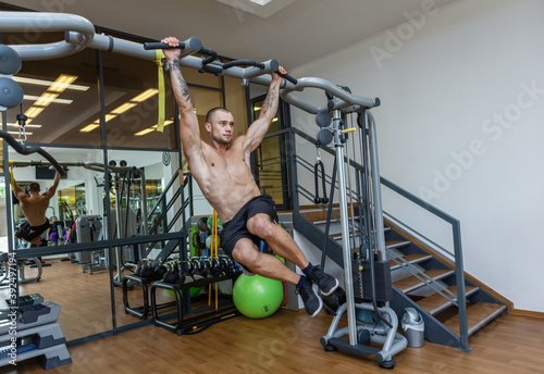 Young muscular fitness man training abdominal muscles while hanging on the horizontal bar in the gym