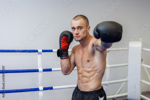 Muscular man with a naked torso trains hand punch with boxing gloves in the ring