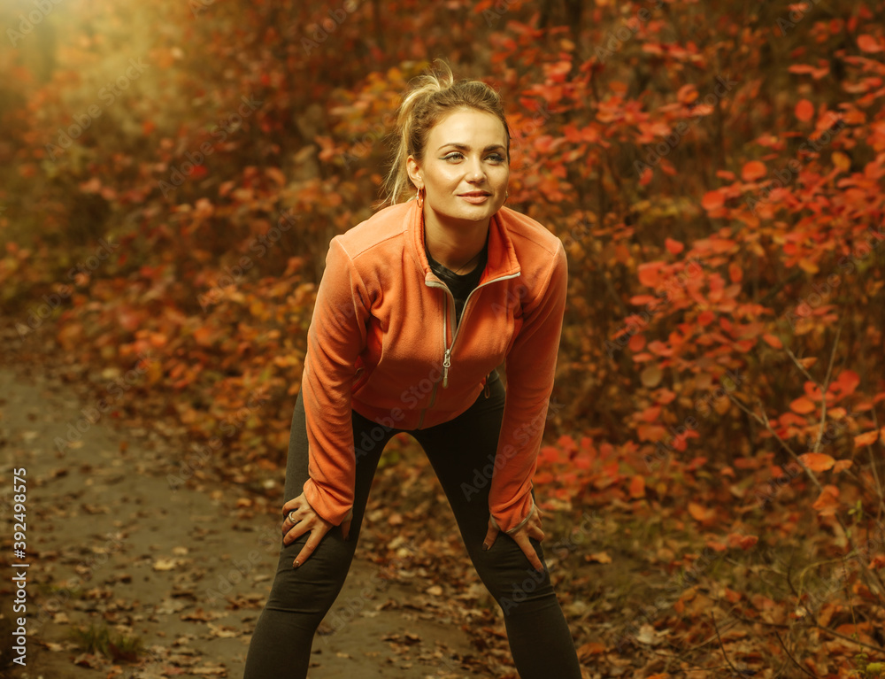 Tired sport woman in sportswear in the autumn forest. Jogging along a path with red leaves. Outdoor sports Tired sport woman in sportswear in the autumn forest. Jogging along a path with red leaves. Outdoor sports