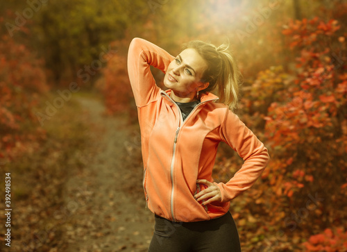 Image of a young fit woman in sportswear in the autumn forest with reddened leaves on the trees