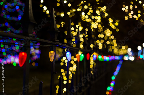 Multicolored lights line a wrought iron fence on a sidewalk