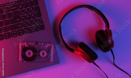 Lptop with headphones and audio cassette. Neon blue-red gradient light. Retro wave, pop culture, DJ equipment. Top view photo