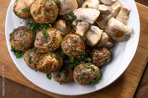 Fried new potatoes with a crust with champignons in a creamy sauce close-up on a wooden board. Appetizing homemade or restaurant food