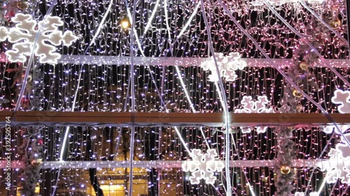 Luminescent bright snowflake coloured light bulbs in light tunnel. Christmas street decorations, new year preparation in city.Abstract blurry background
