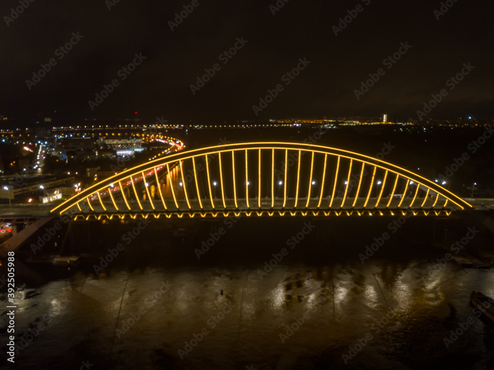 Aerial drone view. Modern arch cable-stayed bridge in Kiev in the evening. Colored lighting of the arch of the bridge.