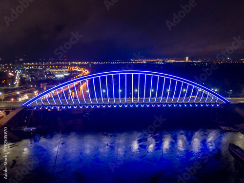 Aerial drone view. Modern arch cable-stayed bridge in Kiev in the evening. Colored lighting of the arch of the bridge. © Sergey