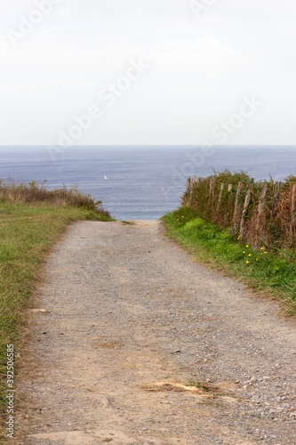 Empty path to the sea. Camino de Santiago concept. Countryside landscape. Trail to the beach along the meadow. Walk and travel concept. Rural nature. Country road in perspective. Calm landscape.