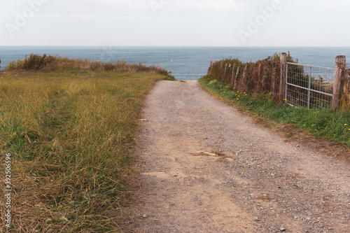 Empty path to the sea. Camino de Santiago concept. Countryside landscape. Trail to the beach along the meadow. Walk and travel concept. Rural nature. Country road in perspective. Calm landscape with o