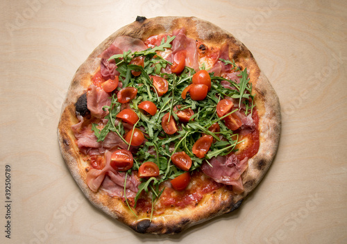 Italian pizza topped with tomato sauce, mozzarella, prosciutto, rocket salad and cherry tomatoes, top view on wooden background