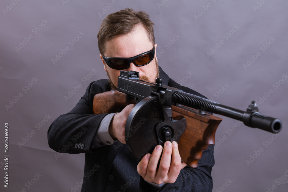 Mature man in sunglasses dressed in suit with tommy gun Mature man in sunglasses dressed in suit with tommy gun