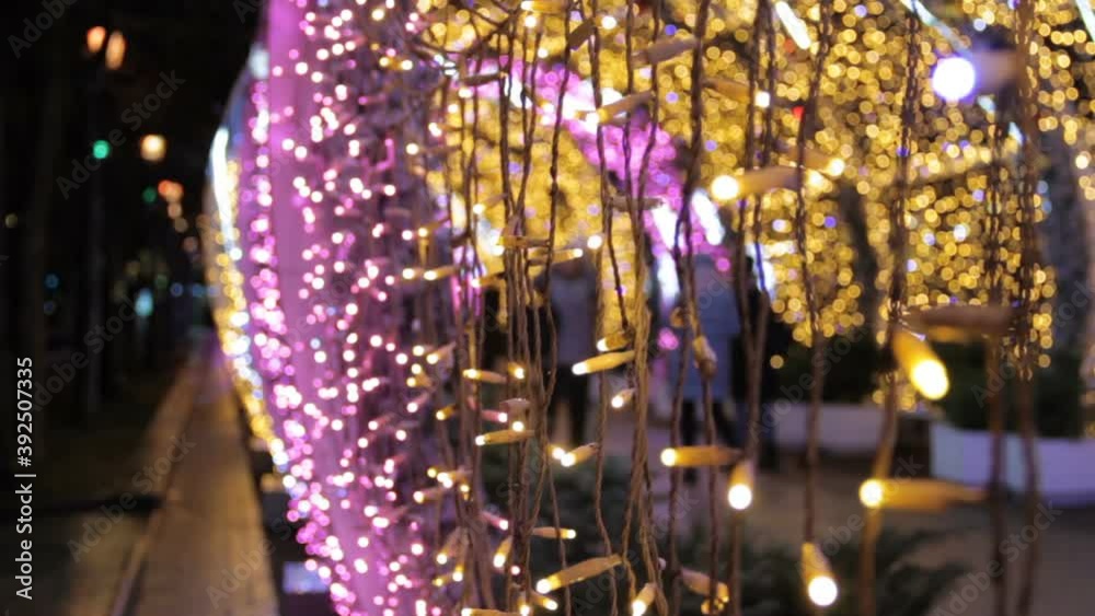 Close up of light bulbs of a garland in light tunnel.Christmas street decorations, new year preparation in city.Alley with blurred shimmering lights.People walk through the light tunnel Close up of light bulbs of a garland in light tunnel.Christmas street decorations, new year preparation in city.Alley with blurred shimmering lights.People walk through the light tunnel