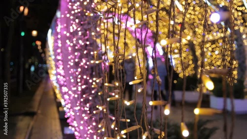 Close up of light bulbs of a garland in light tunnel.Christmas street decorations, new year preparation in city.Alley with blurred shimmering lights.People walk through the light tunnel