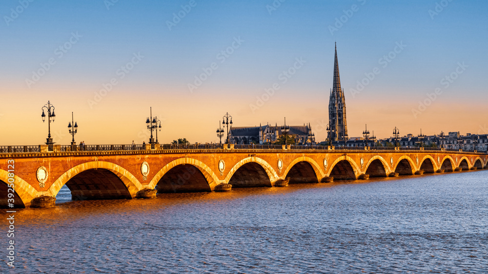 Bordeaux, France. Panoramic view of  Pont de Pierre, old stone bridge over the river Garonne, and Saint Michel cathedral at sunset.