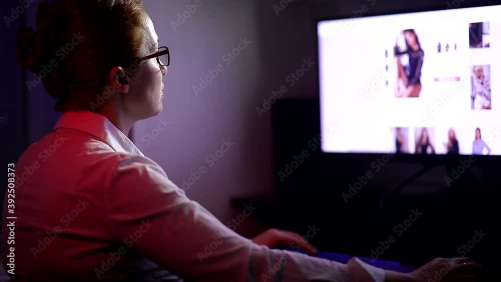 a woman works remotely sitting at home at night at a computer. a woman works remotely sitting at home at night at a computer.