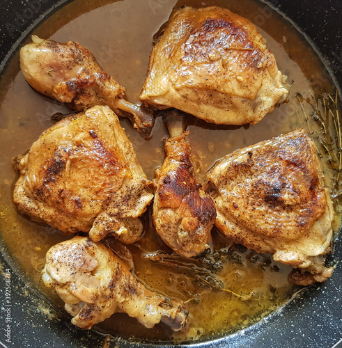 Chicken legs stewed with garlic and thyme. Dish is in black frying pan on the white gas stove