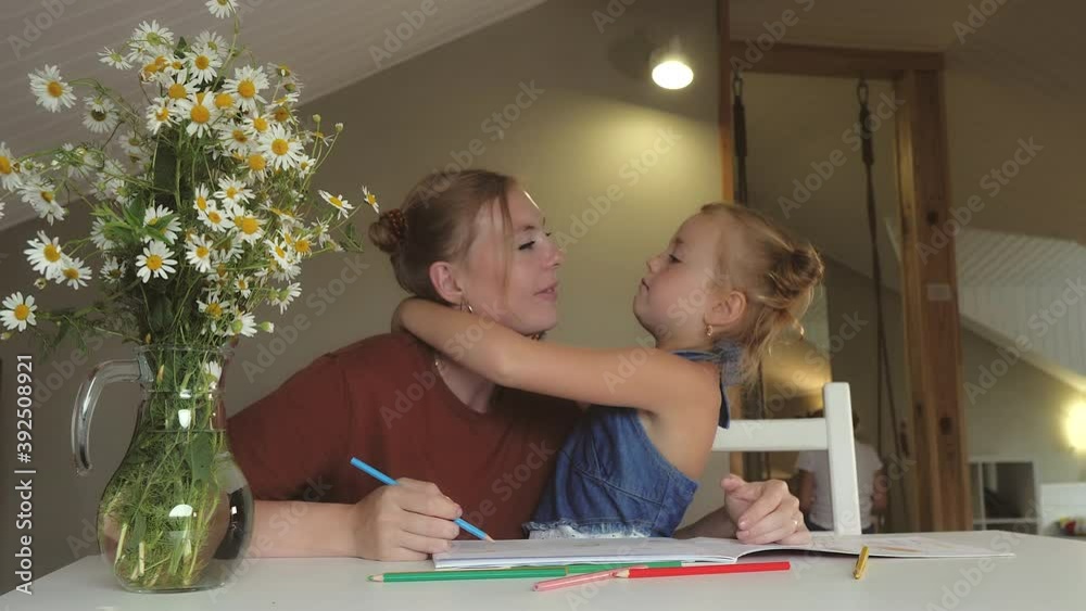 Mom teaches her daughter to draw. Scandinavian family blonde girls with freckles enjoy creative activities at home together. The child shows love for his mother. Large vase of flowers decorate table