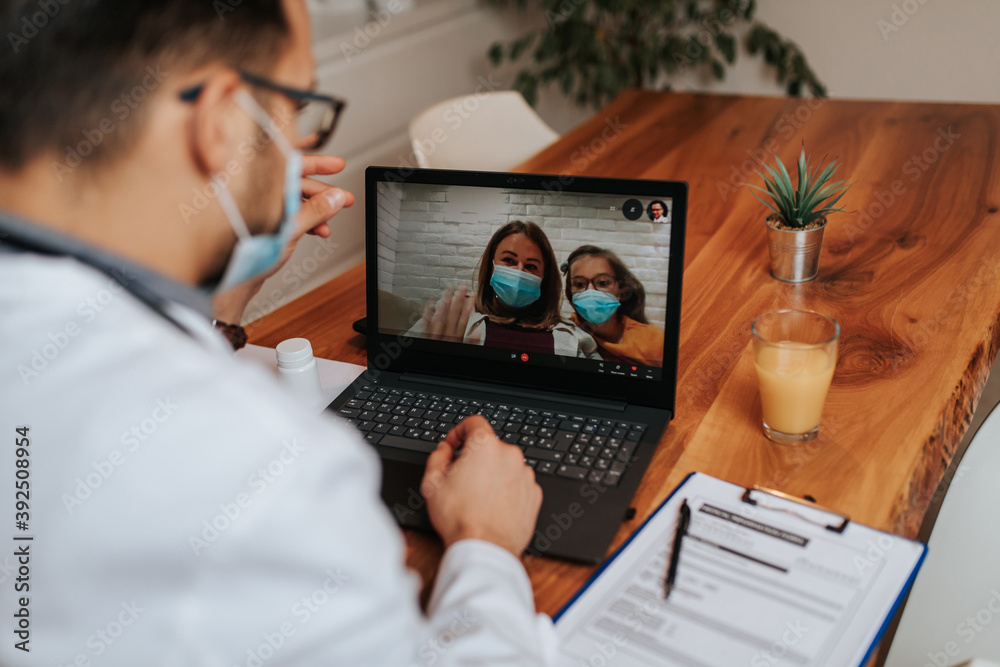 Middle age doctor talking and examining little girl using laptop computer and internet connection. They are chatting while doctor gives health advices. Telehealth concept.