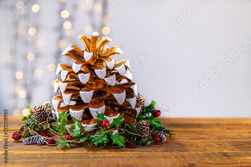 The materials to create a X-mas corner: a gold and white painted pine cone, holly leaves with red berries and little pine cones, a sparkling lights in the background to enhance the wintry atmosphere. photo