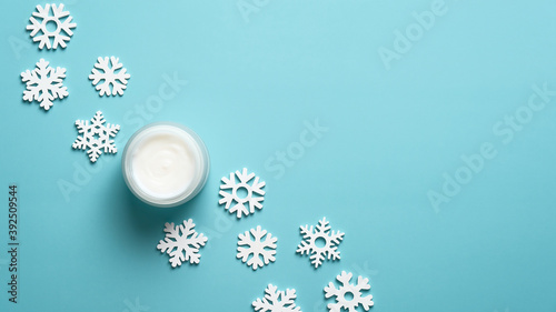 Jar of moisturizer cream and snowflakes on pastel blue background. Winter skin care cosmetics. Flat lay, top view