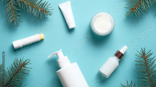 Winter skin care cosmetics. Set of beauty products packaging with Christmas tree branches on pastel blue background. Flat lay, top view.