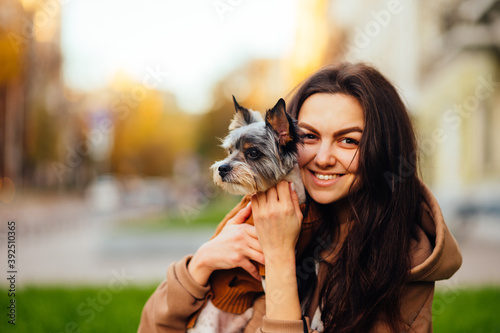 Happy female dog owner hugs pet in her arms and looks at camera and smiles. Lady loves her cute little dog and rejoices, close portrait.