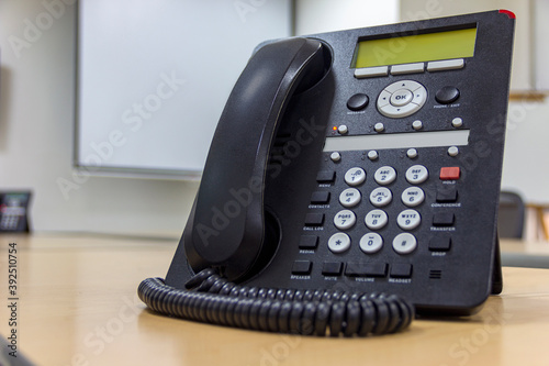 Conference table with office telephone in the foreground, office switch to pass calls to different extensions. Telephone with buttons and numbers.