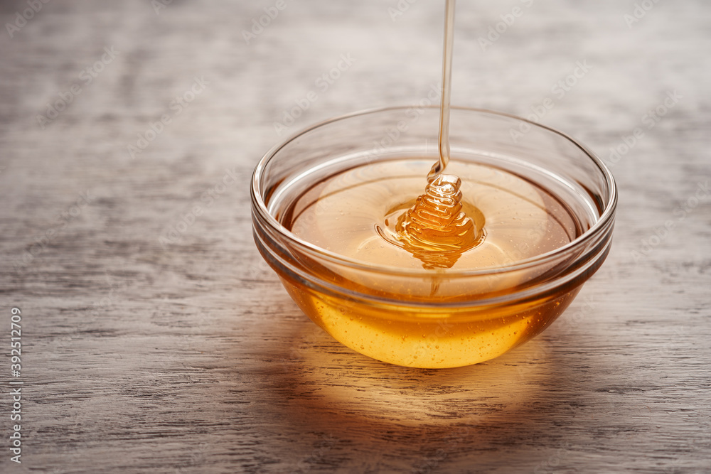 Fresh acacia honey is poured into a transparent bowl near the copy space Fresh acacia honey is poured into a transparent bowl near the copy space