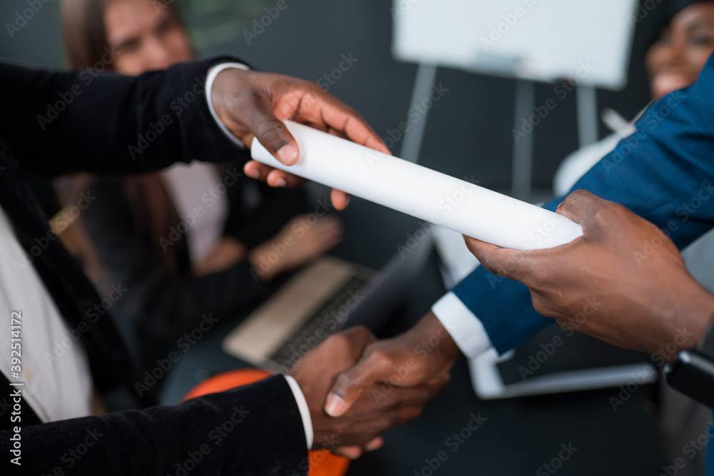 Close-up of a handshake of two African American men. The investor signed the contract and hands it over to the business partner
