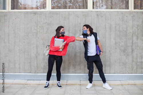 Two university students bump their elbows instead of hug. Avoid the spread of coronavirus, social distance.