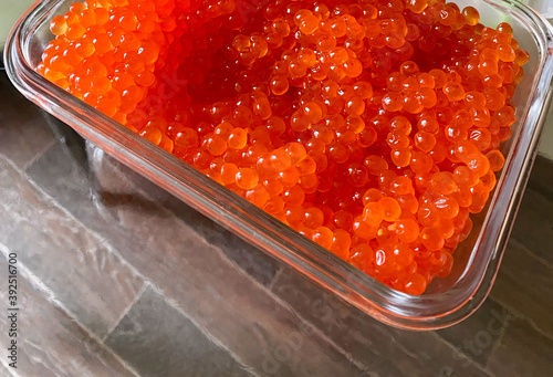 Red salmon caviar in a glass container on a transparent table