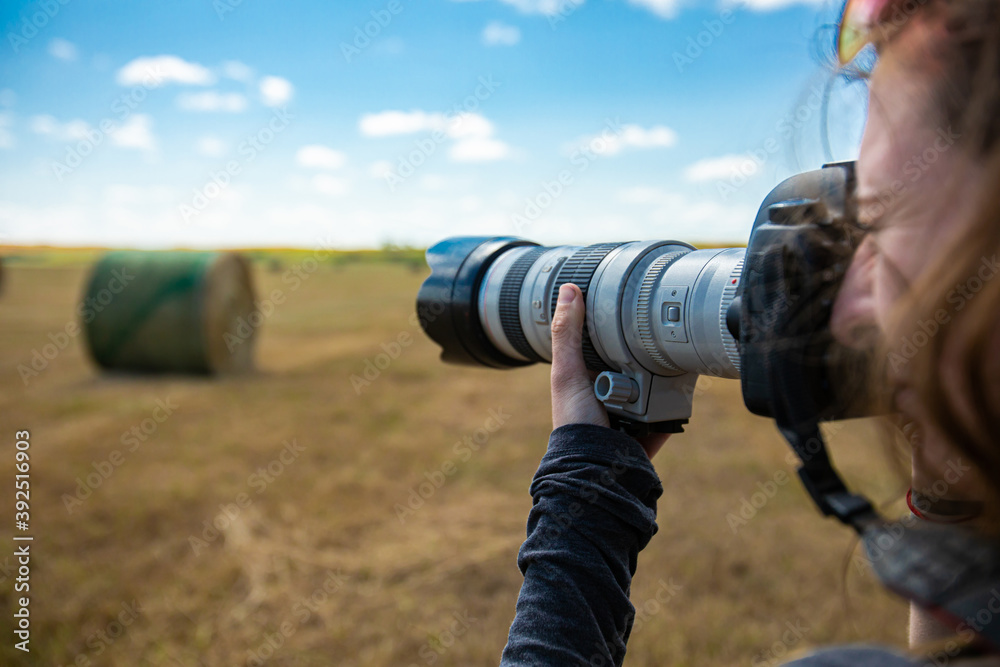Close up shot of a professional DSLR camera equipped with a long telephoto zoom lens held by female photographer during outdoor shooting session. Close up shot of a professional DSLR camera equipped with a long telephoto zoom lens held by female photographer during outdoor shooting session.