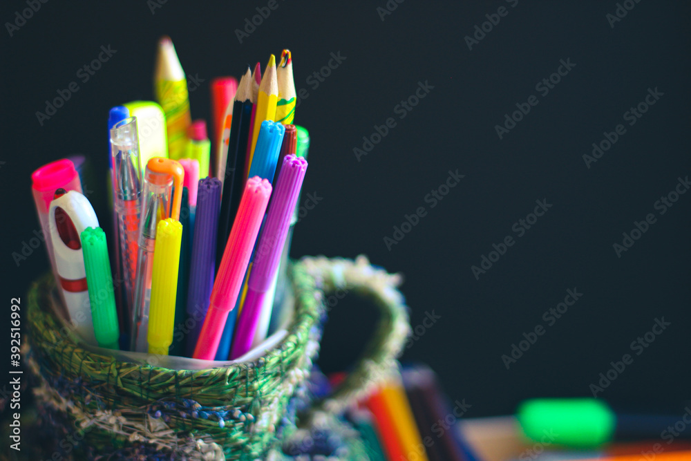 Obraz premium Color pencils and pens on the background of a dark school blackboard. On the board place for a copy space.