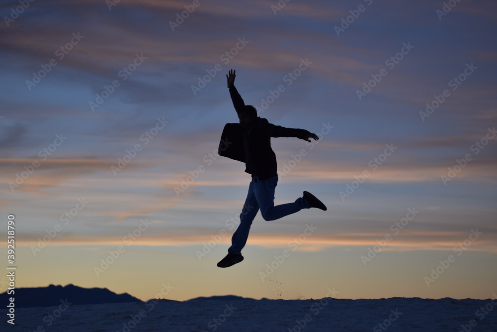 Young energetic happy man jumping high on mountain background and colorful sunset clouds pattern