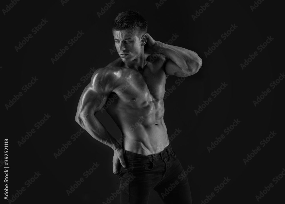 Obraz premium Muscular model sports young man on dark background. Fashion portrait of strong brutal guy. Sexy torso. Male flexing his muscles. Black and white photo.