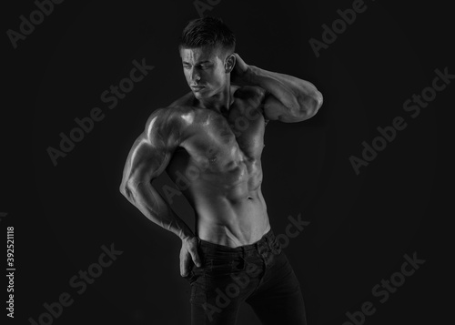 Muscular model sports young man on dark background. Fashion portrait of strong brutal guy. Sexy torso. Male flexing his muscles. Black and white photo.