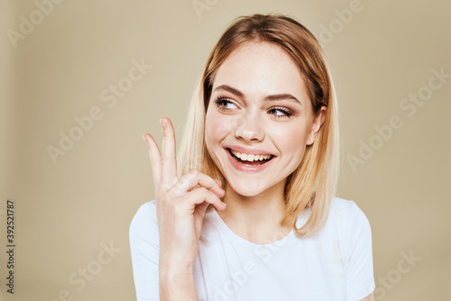 Cheerful blonde woman in a white T-shirt gestures with her hand emotions beige background