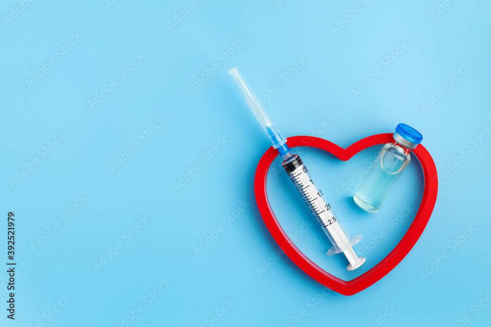 Heart Injection And Vaccine Vial. Covid 19 Cure. Medical Ampoule Dose And Needle On Blue Background, Top View With Copy Space. Heart Injection And Vaccine Vial. Covid 19 Cure. Medical Ampoule Dose And Needle On Blue Background, Top View With Copy Space.