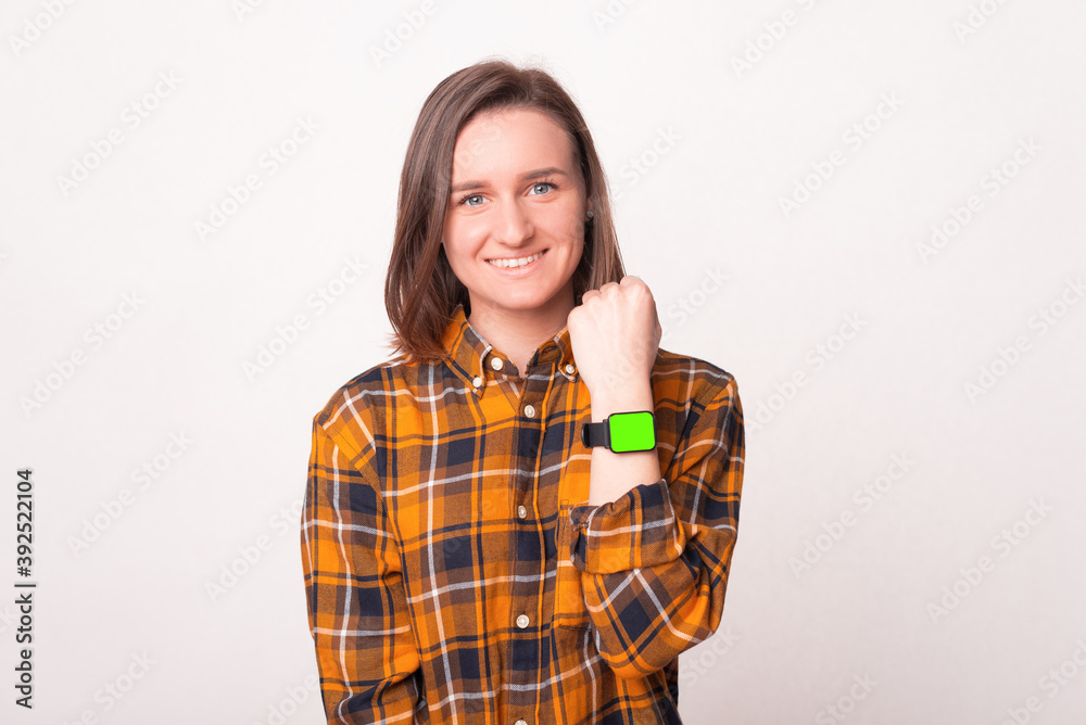 Happy young woman is looking at the camera and smiling having a watch on her hand . Happy young woman is looking at the camera and smiling having a watch on her hand .